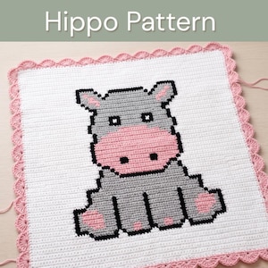 Könnte beinhalten: Eine quadratische Häkeldecke mit einem verpixelten grauen Nilpferd mit rosa Schnauze und Füßen auf weißem Grund. Die Decke ist mit einem rosa Muschelrand versehen. Der Text Hippo Pattern ist oben im Bild zu sehen.