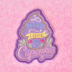 May include: Purple felt cupcake applique with embroidered text "peace love & cupcakes" in various colors.