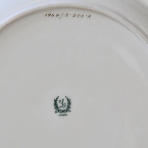 May include: The back of a white ceramic plate with a green Lenox logo and the text "1964/A 310-A" in black.