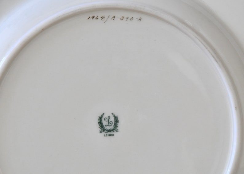 May include: The back of a white ceramic plate with a green Lenox logo and the text "1964/A 310-A" in black.
