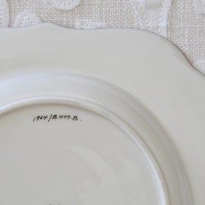 May include: The bottom of a white ceramic plate with a black handwritten inscription that reads "1964/B.407.B."
