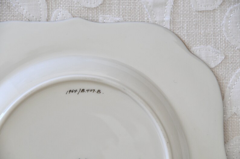 May include: The bottom of a white ceramic plate with a black handwritten inscription that reads "1964/B.407.B."