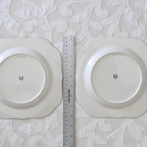 May include: Two white ceramic plates with scalloped edges. The plates have a raised rim and a center well. The back of each plate has a green and white logo.