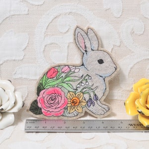 May include: Embroidered patch of a gray bunny with pink, yellow, and green flowers. The bunny is about 3 inches tall.