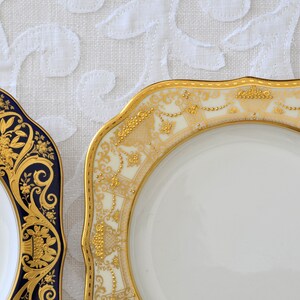 May include: Two decorative plates with gold and white designs. One plate has a blue rim and the other has a cream rim.
