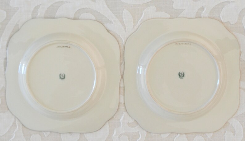 May include: Two white square-shaped plates with scalloped edges. The plates have a raised rim and a center well. The back of each plate has a green and black crest with the text "MADE IN USA".