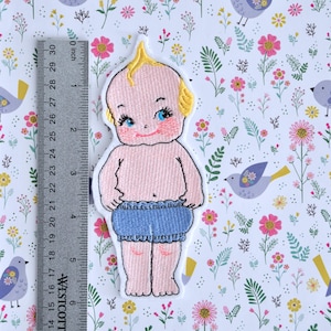 May include: Embroidered iron-on patch of a baby doll with blonde hair, blue eyes, and wearing a blue diaper. The patch is approximately 2 inches tall.