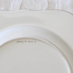 May include: The bottom of a white ceramic plate with the inscription "1964/A 310-A" in black ink.