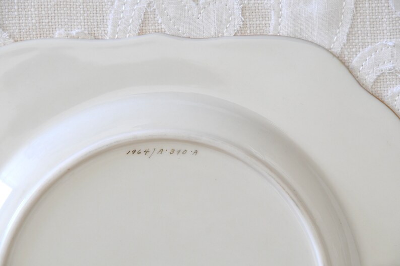 May include: The bottom of a white ceramic plate with the inscription "1964/A 310-A" in black ink.