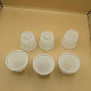May include: A set of six translucent white plastic molds for food preparation. Three molds are positioned with their fluted sides and star-patterned bases facing upward, while three are placed with their flat, circular lids facing upward.