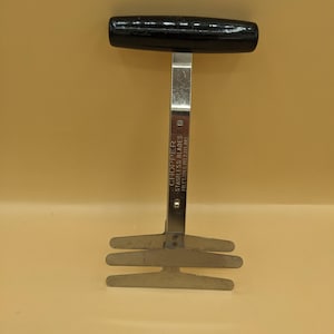 May include: A kitchen chopper with a black horizontal handle and a vertical metal shaft. The shaft features the text CHOPPER STAINLESS BLADES FOLEY MFG PAT 2,113,085. At the base, there are three parallel metal blades for cutting food items.