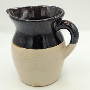 May include: A small, brown and white ceramic pitcher with a handle. The pitcher has a crackled glaze on the white portion.