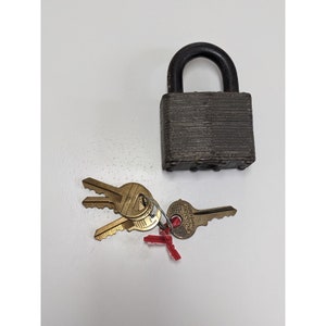 May include: A vintage padlock with a black metal body and a silver keyhole. The padlock is accompanied by three keys with brass heads and silver shafts.