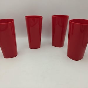 May include: Four red plastic tumblers are arranged on a white surface. The tumblers are tall, with a slightly oval top and a rectangular base. The color is a vibrant, solid red.
