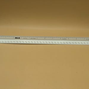 May include: Two white and gray architectural rulers. The top ruler is gray and the bottom ruler is white. The rulers are marked with measurements in inches and centimeters. The word "HELIX" is printed on the top ruler.