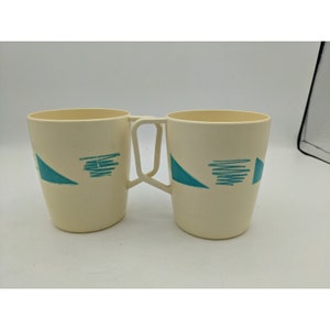 May include: Two white ceramic mugs with blue geometric designs. The mugs are connected by a handle.