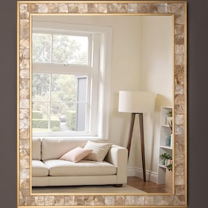 May include: A rectangular wall mirror featuring a wide frame composed of small, square, iridescent shell tiles in shades of beige and tan. The frame is bordered by thin gold-toned metal edges, providing a structured and reflective surface.