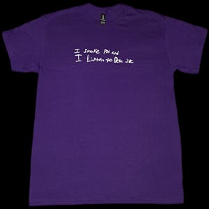 May include: A purple t-shirt with white handwritten text that reads "I Smoke Pot and I Listen to Pete Jive". The shirt is made of a soft material and has a crew neck.