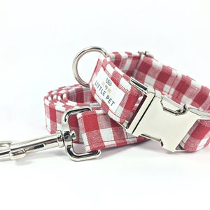May include: Red and white gingham dog collar and leash set with silver hardware. The collar has a silver buckle and a tag that reads "The Little Pet".