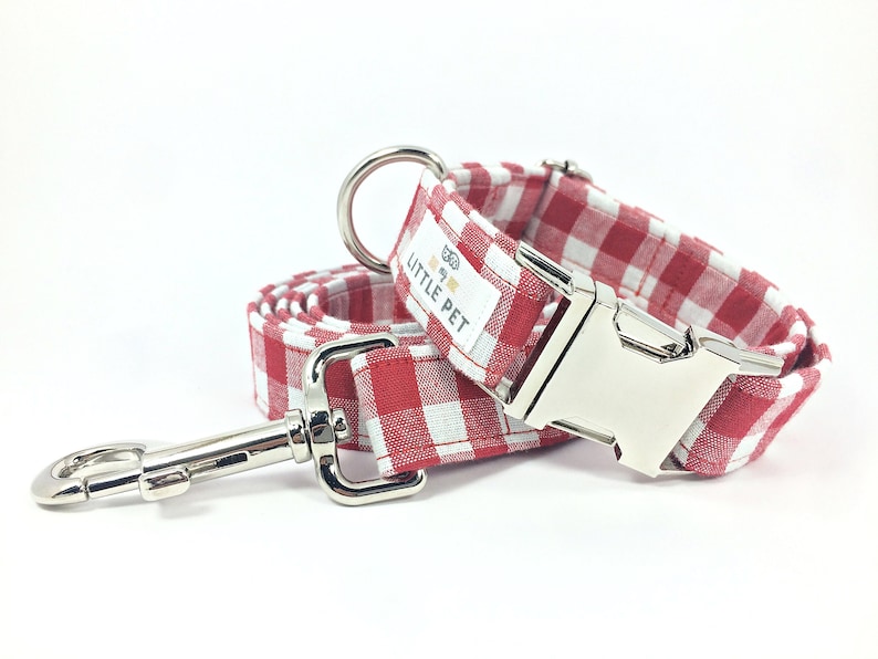 May include: Red and white gingham dog collar and leash set with silver hardware. The collar has a silver buckle and a tag that reads "The Little Pet".
