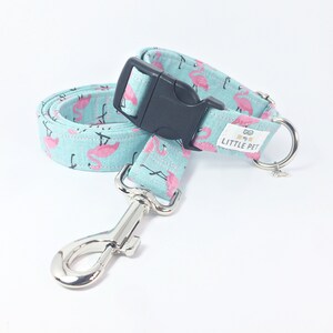 May include: A light blue dog collar and leash set with a pink flamingo print. The collar has a black buckle and a silver D-ring. The leash has a silver hook.