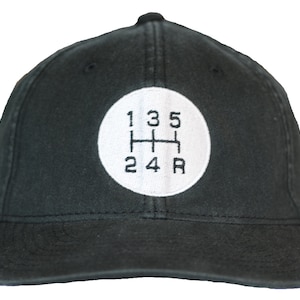May include: Black baseball cap with a white circle and black embroidered text that reads "1 3 5 2 4 R" resembling a car's gear shift pattern.