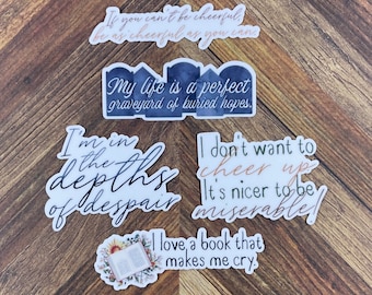 Op de afbeelding: Vijf stickers met verschillende citaten. De citaten zijn: "Als je niet vrolijk kunt zijn, wees dan zo vrolijk als je kunt", "Mijn leven is een perfecte begraafplaats van begraven hoop", "Ik ben in de diepte van wanhoop", "Ik wil niet opvrolijken, het is fijner om ellendig te zijn", en "Ik hou van een boek dat me aan het huilen maakt".