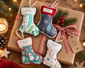 May include: Four small fabric Christmas stockings with hanging loops. One features green foliage, one has a dark blue background with snowflakes and trees, one displays gingerbread men and candy canes, and one has colorful Merry Christmas text.