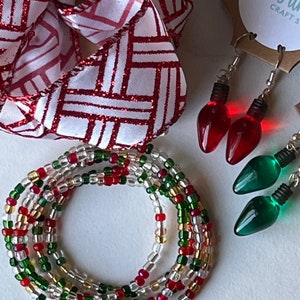 May include: A multi-strand beaded bracelet with red, green, gold, and clear beads. The bracelet is wrapped around itself in a circle. There are also two pairs of earrings in the image. One pair is red and shaped like light bulbs. The other pair is green and shaped like light bulbs. The text "Sunshine Crafts" is visible in the image.