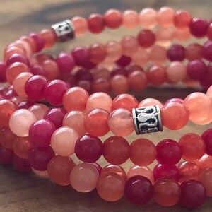 May include: A set of three beaded bracelets in shades of red, orange, and pink. The bracelets are made of small, round beads and feature silver-colored cylindrical spacers with a decorative design. The beads are arranged in multiple strands.