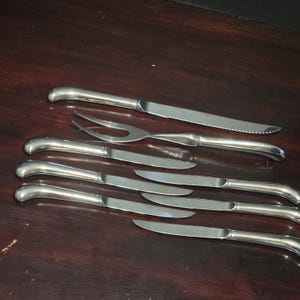 Puede incluir: Un juego de ocho cuchillos para carne plateados y un tenedor a juego con mangos curvos.
