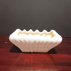 May include: White ceramic planter with a fluted design and a square shape. The planter has a light brown interior.