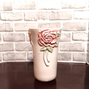 Könnte beinhalten: Eine weiße Keramikvase mit einem rosa-grünen Blumendesign. Die Vase hat ein Reliefdesign aus Rosen mit Blättern und Stielen.