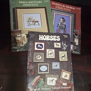 May include: A collection of horse-themed needlepoint books. Titles include "Mares and Foals" and "Horses In Motion." The book "Horses" features various framed horse designs. The books are designed by Judy Nason and Stephanie Seabrook Hedgepath.