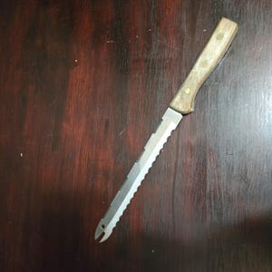May include: A serrated bread knife with a wooden handle. The stainless steel blade has a series of sharp teeth along one edge and a pointed tip. The handle is light brown and secured with brass rivets.