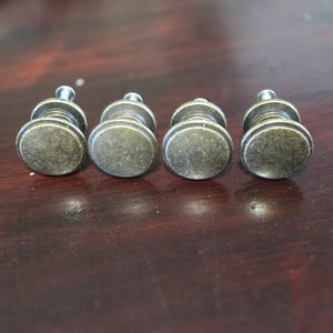 Op de afbeelding: Vier antieke goudkleurige kastknoppen met een rond, licht verhoogd, getextureerd oppervlak. De knoppen hebben een eenvoudig ontwerp en zijn ideaal om meubels een vintage uitstraling te geven.
