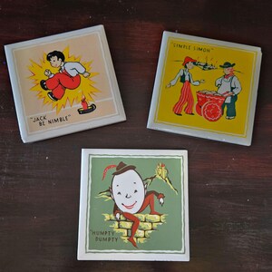 以下が含まれることがあります： 童謡をテーマにしたヴィンテージのセラミックタイル3枚。タイルは白地にカラフルなイラストとテキストが描かれています。最初のタイルには、ろうそくの上を跳ねる少年が描かれており、「ジャック・ビー・ニンブル」というテキストが書かれています。2枚目のタイルには、2人の少年が描かれており、「シンプル・サイモン」というテキストが書かれています。3枚目のタイルには、大きな頭をしたキャラクターが描かれており、「ハンプティ・ダンプティ」というテキストが書かれています。