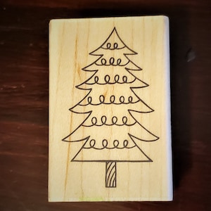 Könnte beinhalten: Ein Holzstempel mit einer schwarzen Umrandung eines Weihnachtsbaums mit einer Lichterkette.
