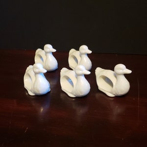 May include: Set of six white ceramic duck napkin rings. The ducks are in a sitting position with their heads turned to the side.