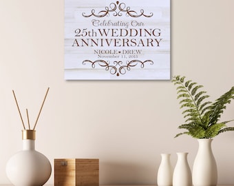 May include: White wooden sign with brown text that reads "Celebrating Our 25th Wedding Anniversary Nicole & Drew November 11, 2015". The sign has a decorative border.