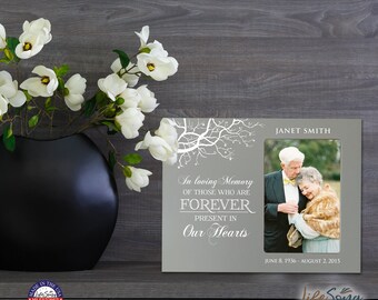 May include: A gray picture frame with a white tree design and the text "In loving memory of those who are forever present in our hearts". The frame has a photo of an older couple and the text "Janet Smith June 8, 1936 - August 2, 2015".