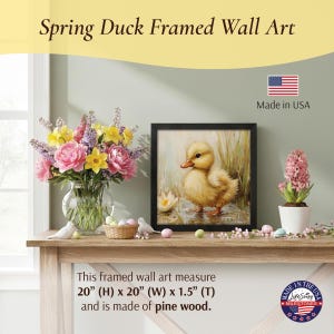 May include: Black framed wall art featuring a yellow duckling in a pond. The art is displayed on a wooden table with a vase of flowers, a potted plant, and decorative eggs. The art measures 20" (H) x 20" (W) x 1.5" (T) and is made of pine wood.