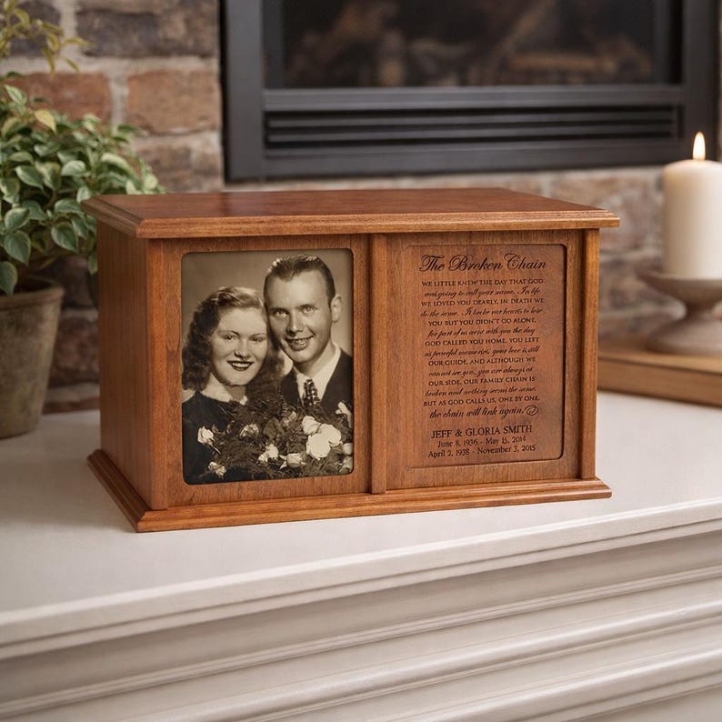 May include: A wooden memorial box with a framed black and white photo of a couple. The box has a sliding panel with engraved text, including the names Jeff & Gloria Smith and dates. A candle and plant are in the background.
