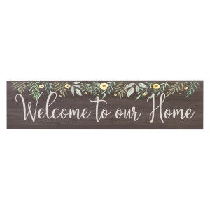 May include: A wooden sign with a brown woodgrain background and a white floral garland with yellow flowers. The sign says "Welcome to our Home" in white script.