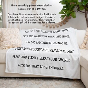 May include: White throw blanket with black text that reads "May love and laughter light your days and warm your heart and home. May God and faithful friends be yours wherever you may roam. May peace and plenty bless your world with joy that long endures."