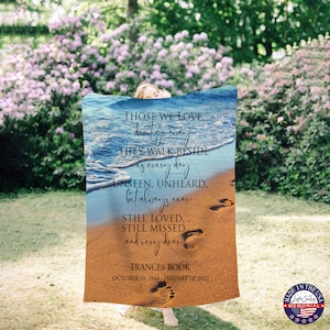 May include: A blue and brown memorial blanket with a beach scene and the text "Those we love, don't go away, they walk beside us every day, unseen, unheard, but always near, still loved, still missed and very dear. Frances Book, October 11, 1944 - January 24, 2022".