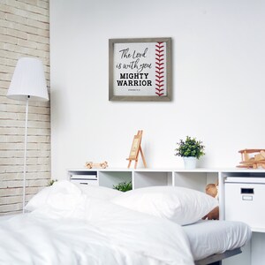 May include: A framed wood sign with a baseball stitch design and the text "The Lord is with you Mighty Warrior, Judges 6:12".