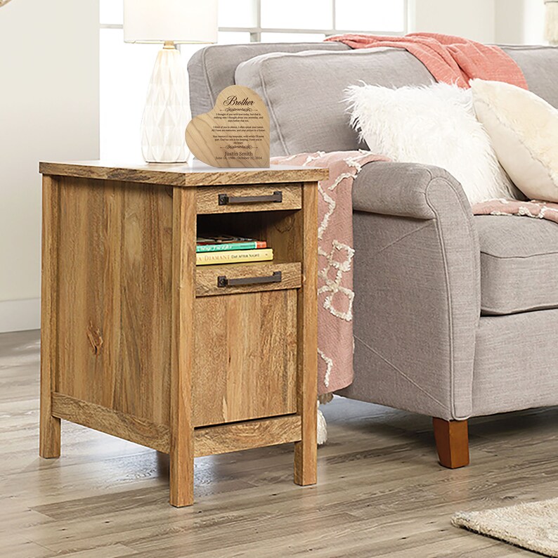 May include: A wooden end table with a drawer and a shelf. The table is light brown in color and has a rustic finish. A heart-shaped wooden plaque with a message about brothers is on top of the table.