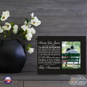 May include: Black picture frame with a photo of an older couple sitting on a bench. The frame has a white inscription that reads "Nuestra Vida Juntos" and lists the number of years, months, weeks, days, and hours they have been together. The inscription ends with "Feliz Aniversario".
