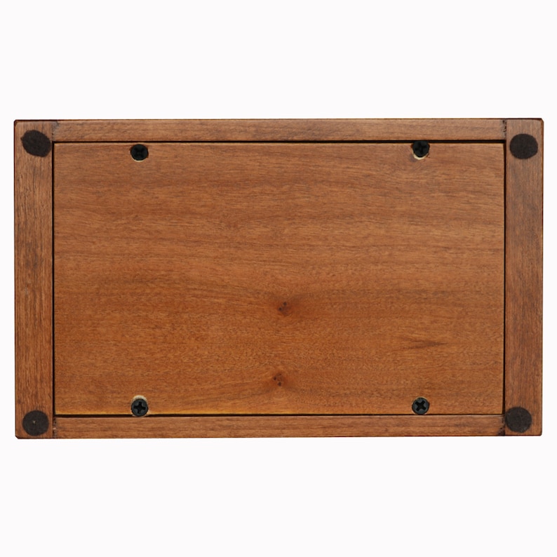 Puede incluir: La parte inferior de una caja de madera, te&ntilde;ida de marr&oacute;n. La caja tiene cuatro tornillos negros en la parte inferior.